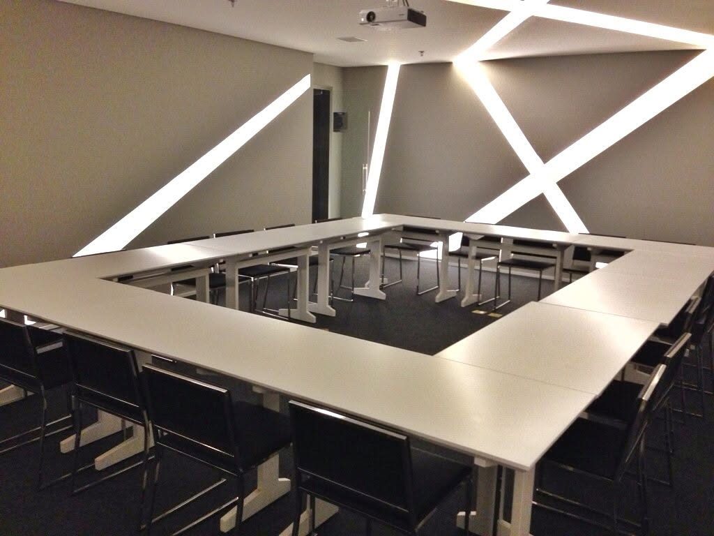 Sala de reuniões com mesas brancas em formato de U e projetor